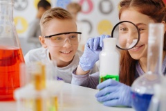 Cheerful girl examining substance in flask with magnifying glass